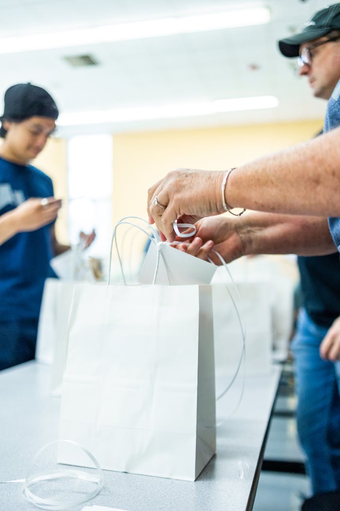 People packing white paper bags at a table indoors, collaborative setting.
